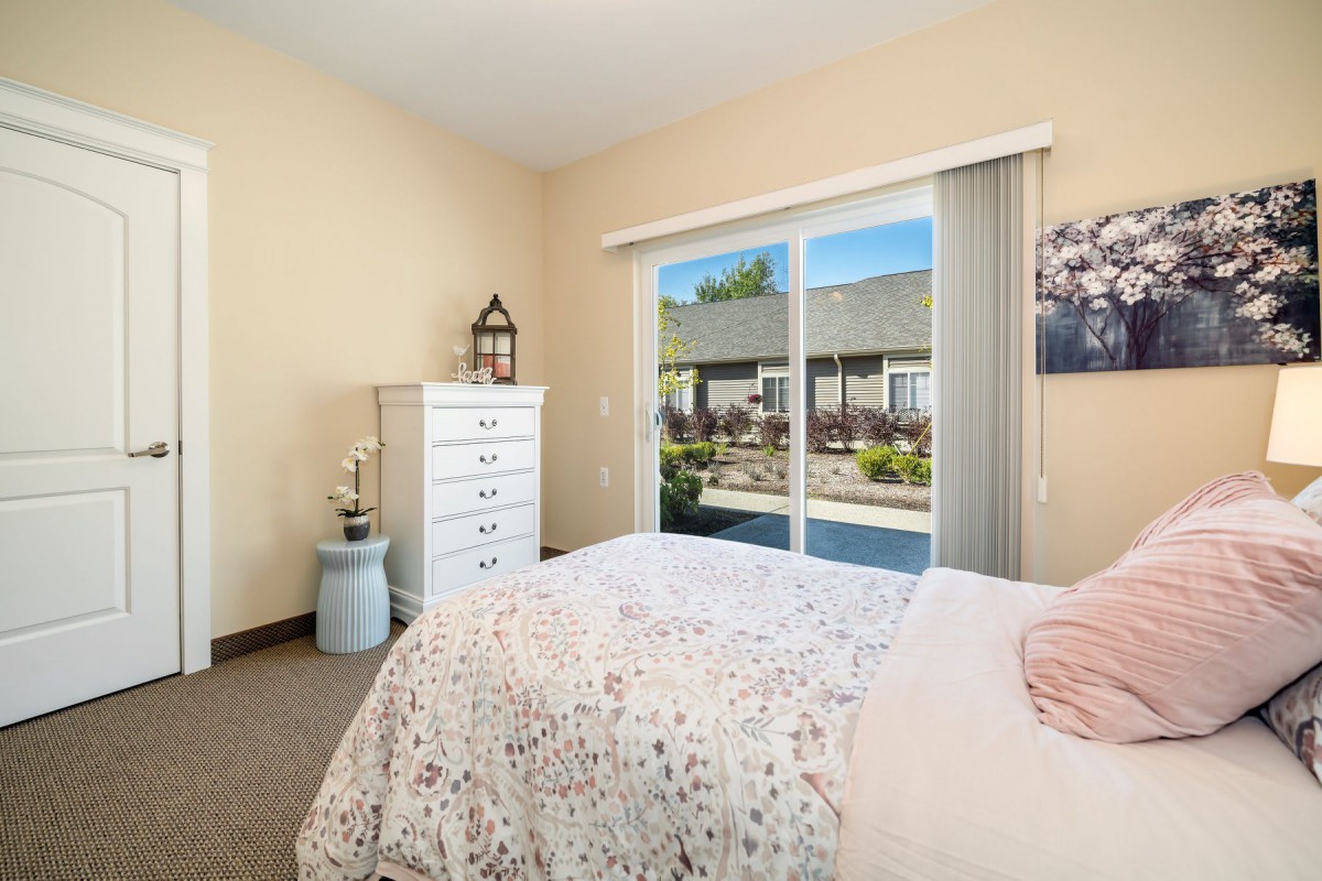 A cozy bedroom with a bed, chest of drawers, and sliding glass door leading to an outdoor view.