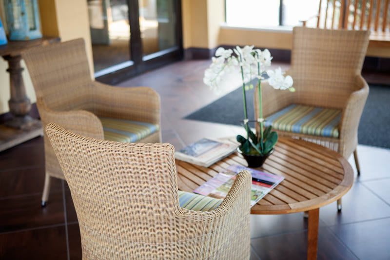 A cozy waiting area with wicker chairs and a wooden table featuring an orchid centerpiece.