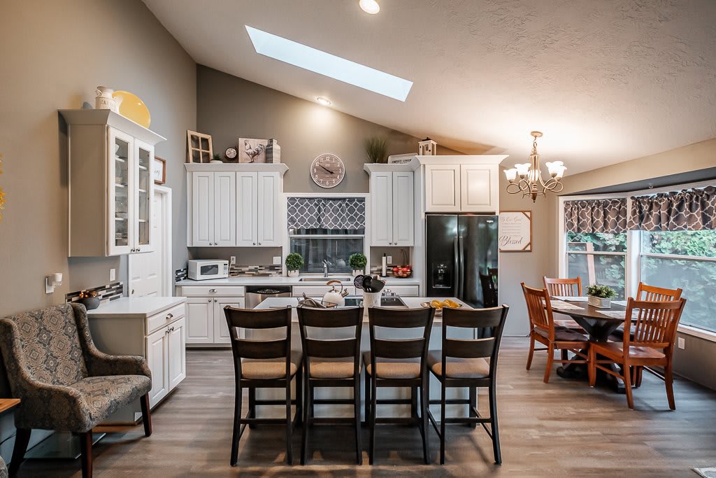 A modern kitchen with white cabinets, an island counter, and skylight, featuring an open concept design with a dining area.