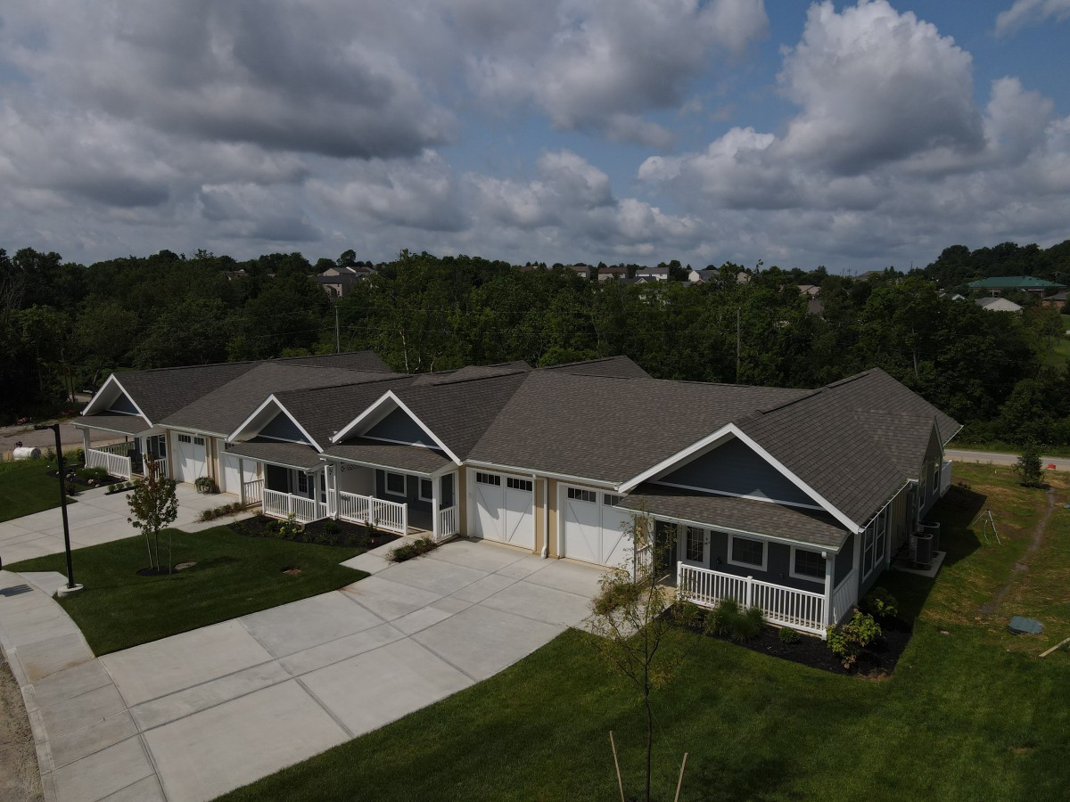 A row of suburban duplexes with a shared driveway and well-maintained lawns under a cloudy sky.