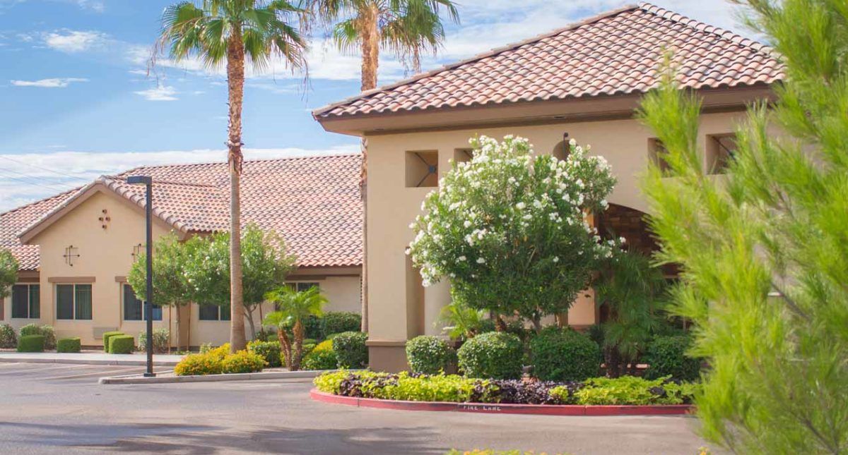 A suburban house surrounded by palm trees and well-maintained landscaping on a sunny day.