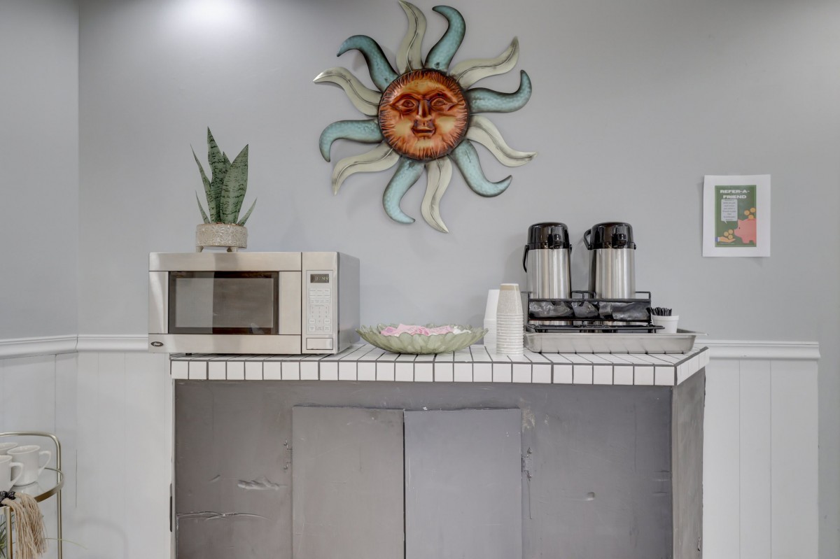 A small kitchen setup featuring a microwave, coffee makers, and decorative sun wall art.
