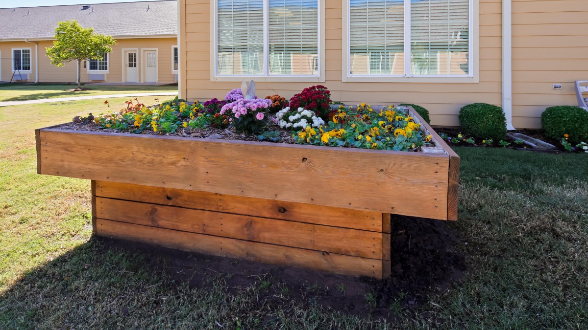 A wooden raised garden bed filled with colorful flowers in front of a house.