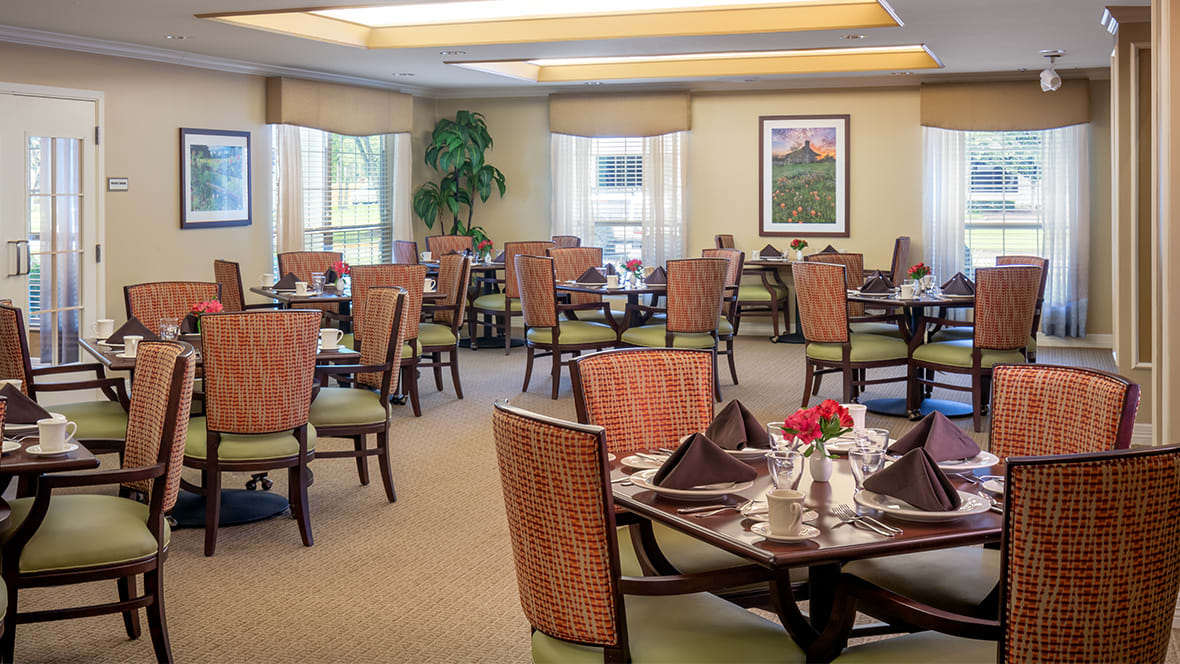 A well-appointed dining room with neatly arranged tables and chairs, featuring large windows and tasteful decor.