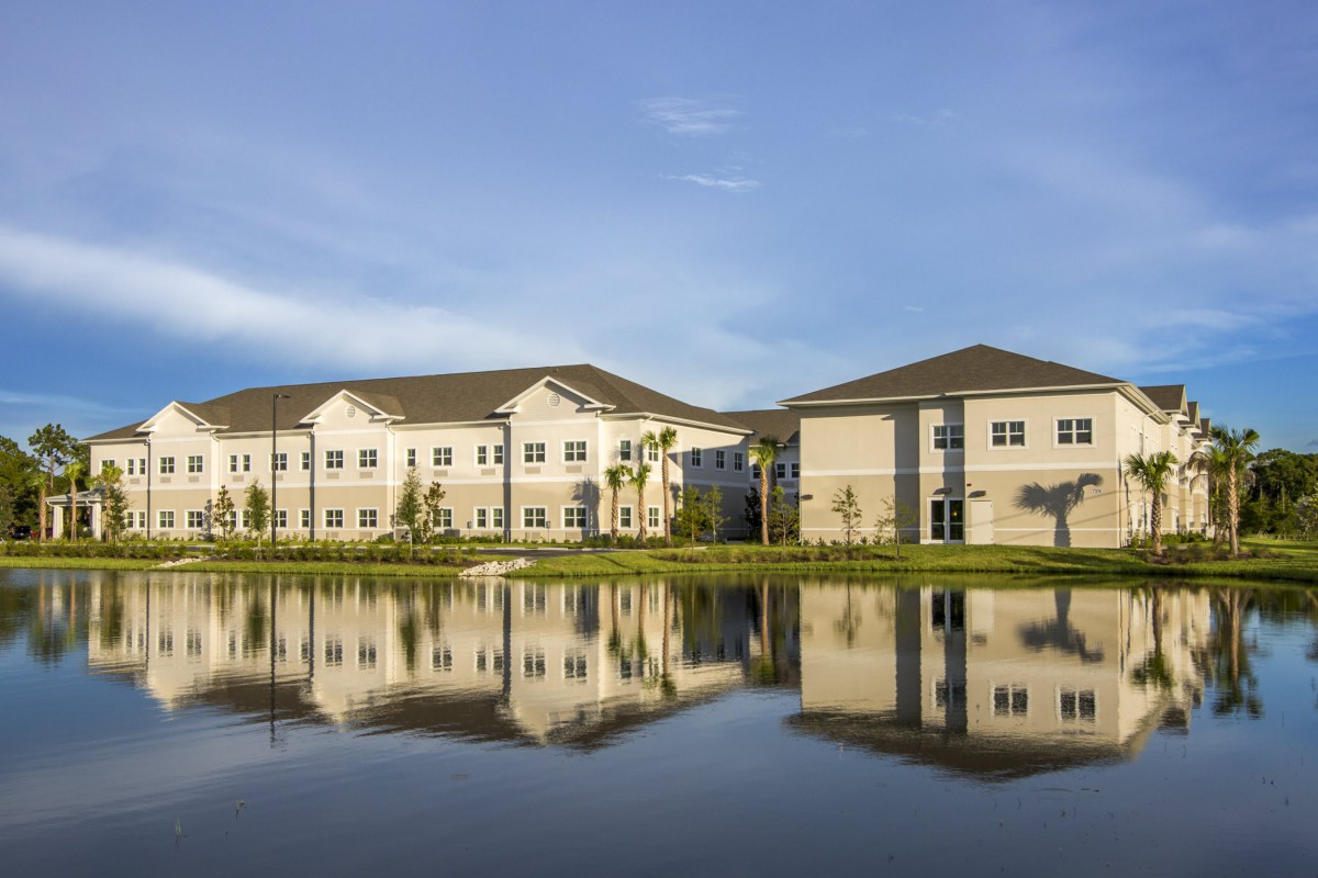 A modern building reflected in a calm lake under a blue sky.
