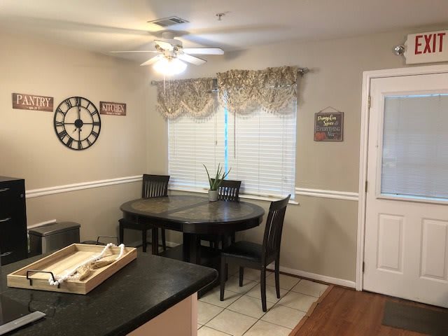 A cozy dining area with a round table, surrounded by chairs, under soft lighting and decorated with a wall clock.