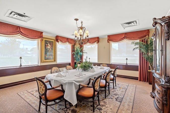An elegantly decorated dining room with a large table set for a meal, surrounded by chairs and illuminated by a chandelier.