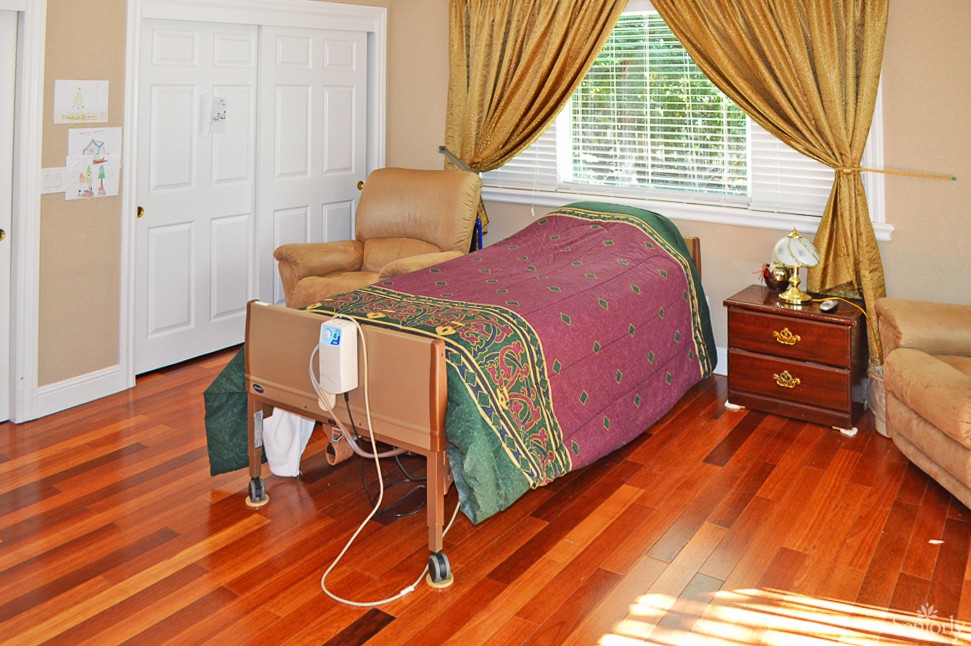 A cozy bedroom with a hospital bed, featuring wooden flooring and elegant curtains.
