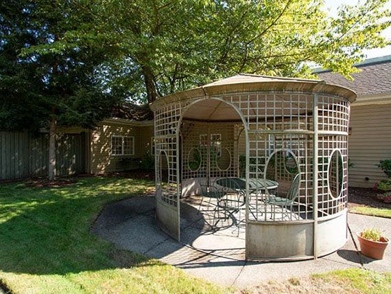 A charming outdoor gazebo surrounded by greenery and shaded by trees.