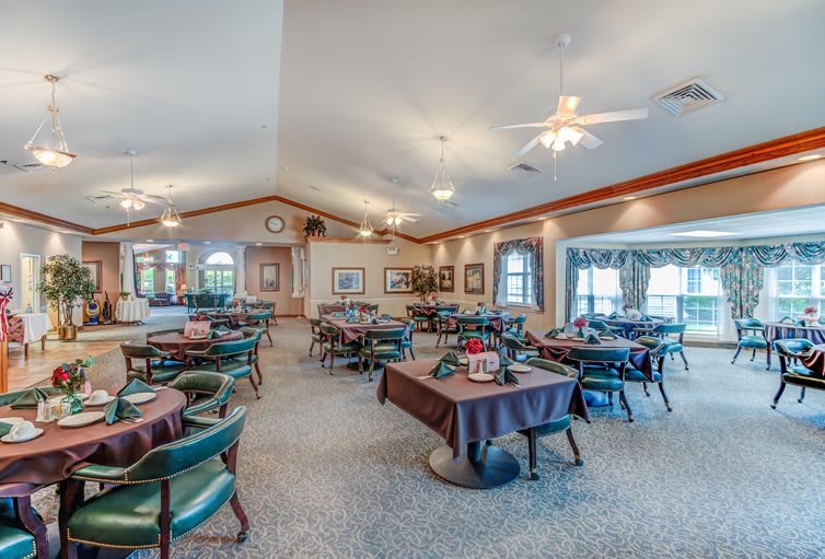 A spacious dining area with multiple tables and chairs, decorated with ceiling fans and artwork on the walls.