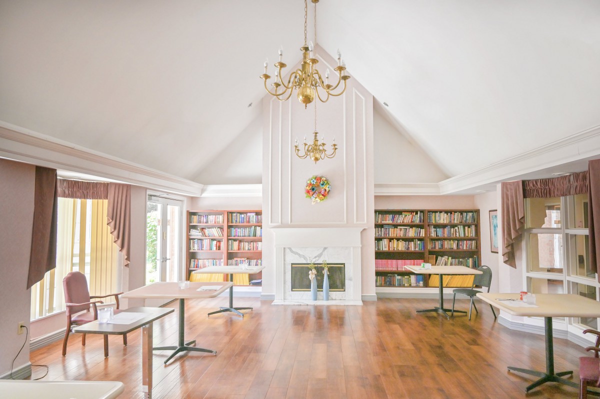 A spacious library with a high ceiling, featuring a central fireplace, elegant chandelier, and bookshelves filled with books.