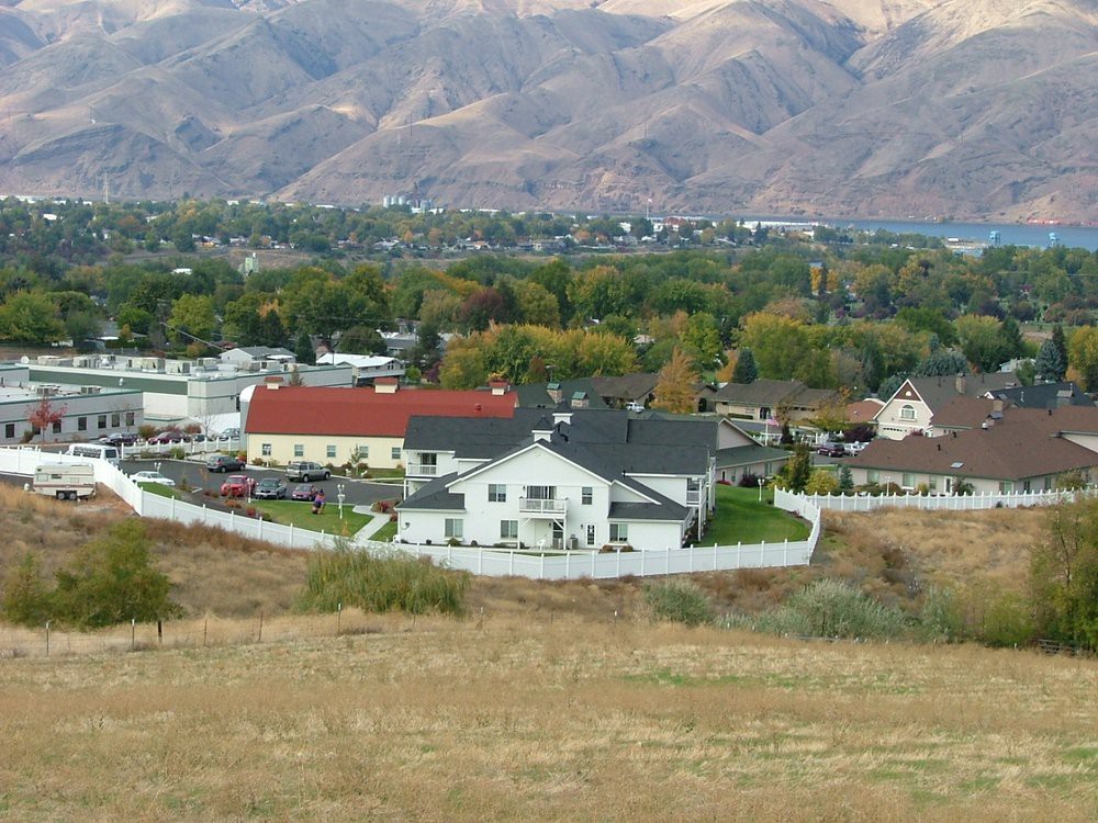 A suburban landscape with houses, a white fence, and mountains in the background.