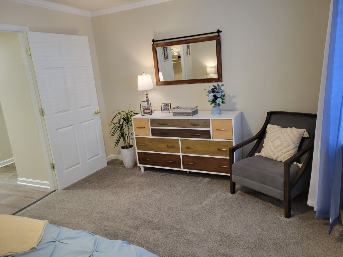 A cozy bedroom with a dresser, mirror, and upholstered chair.