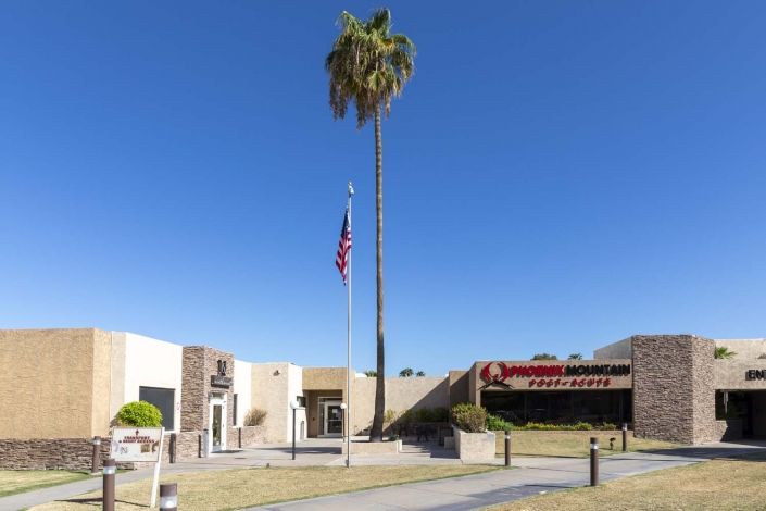 Exterior of a museum with a palm tree and American flag against a clear blue sky.