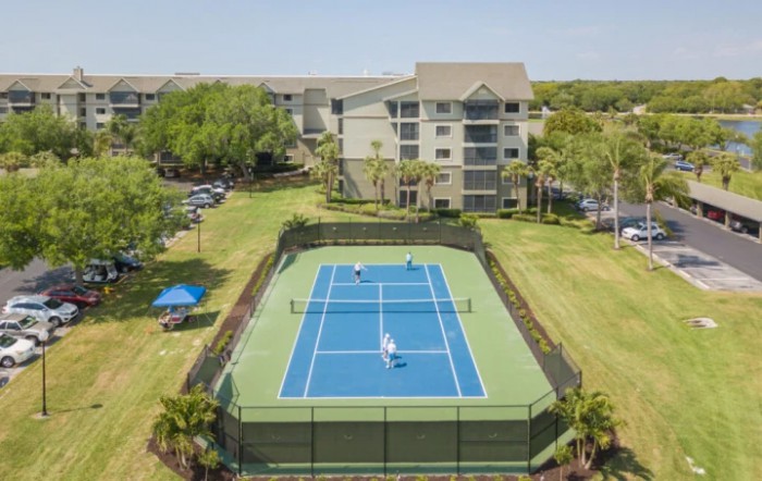 Aerial view of a tennis court situated next to a multi-story residential building.