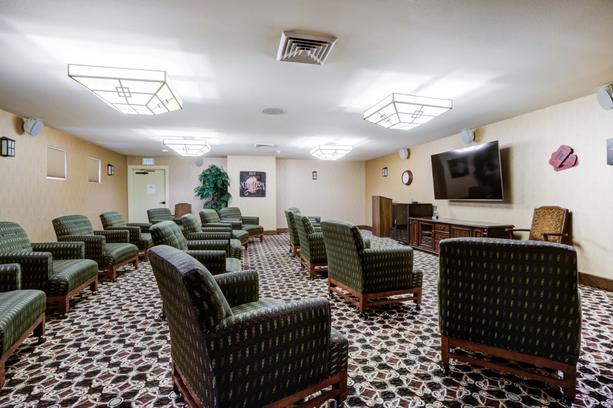 A cozy lounge area with armchairs and a television, featuring patterned carpeting and modern ceiling lighting.