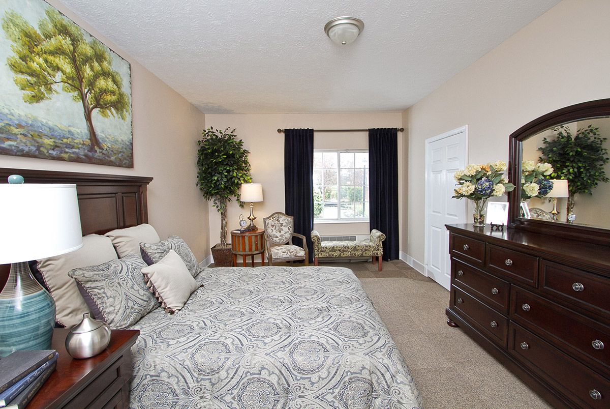 A well-furnished bedroom with a patterned bedspread, dresser, and seating area by the window.