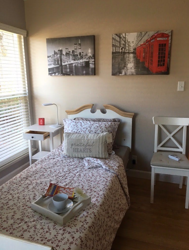 A cozy bedroom with a single bed, decorated with paintings and soft lighting.