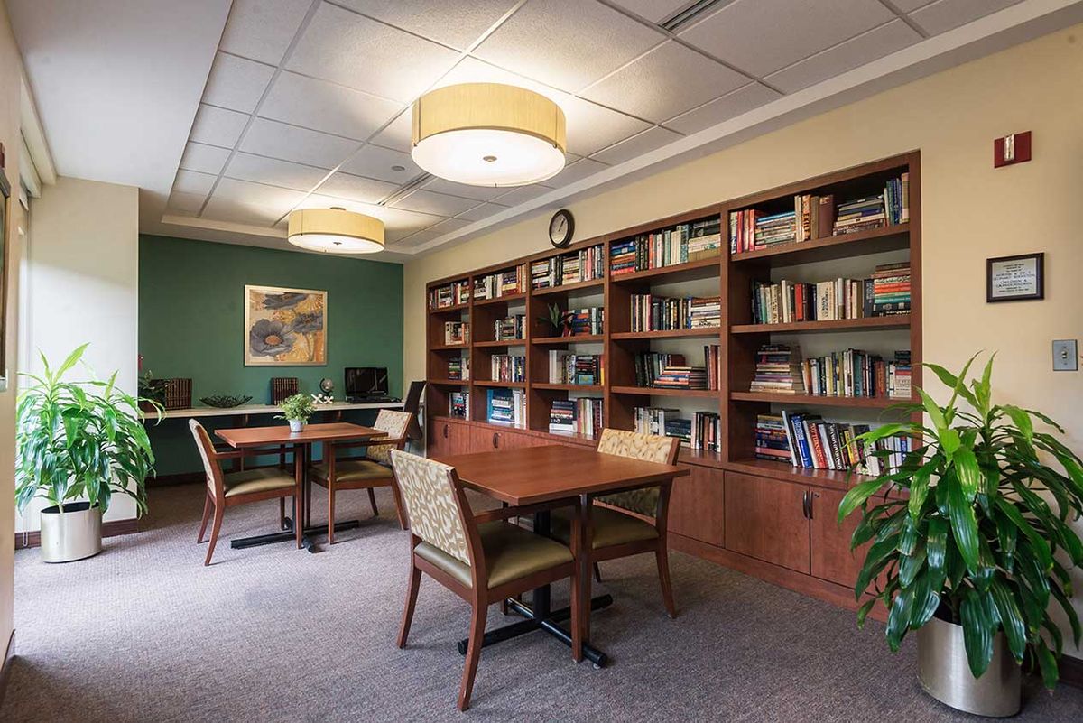 A cozy library reading area with wooden bookshelves, tables, and chairs.