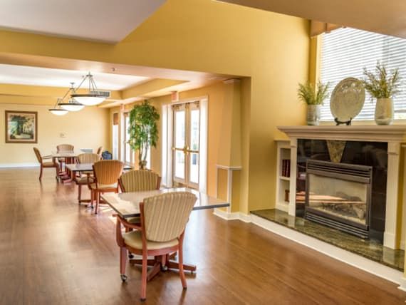 A cozy dining area with tables and chairs, featuring a fireplace and wooden flooring.