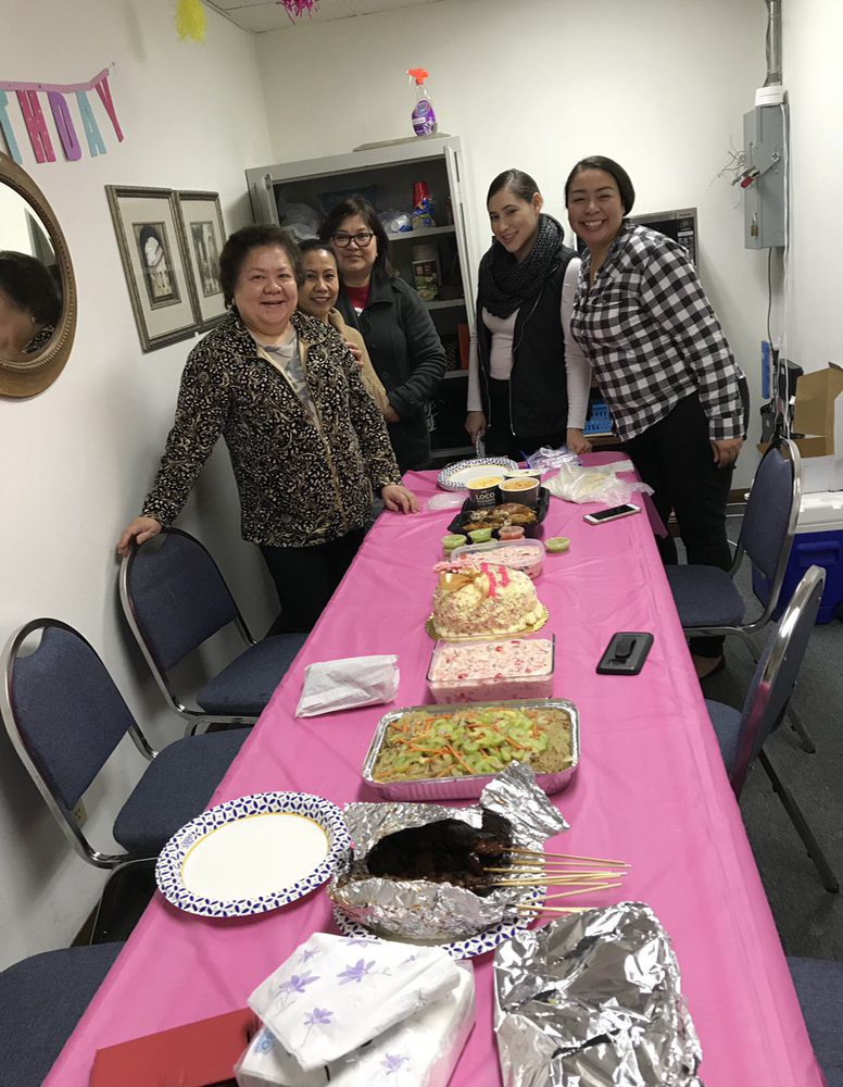 A group of people standing around a table with a variety of food, suggesting a celebration or gathering.