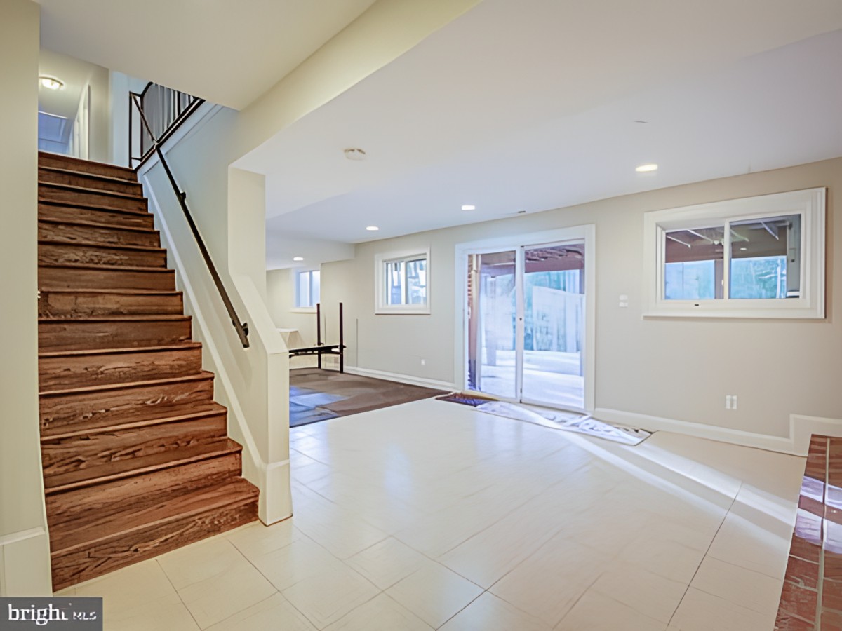 A spacious basement with tiled flooring, stairs leading up, and ample natural light from large windows.