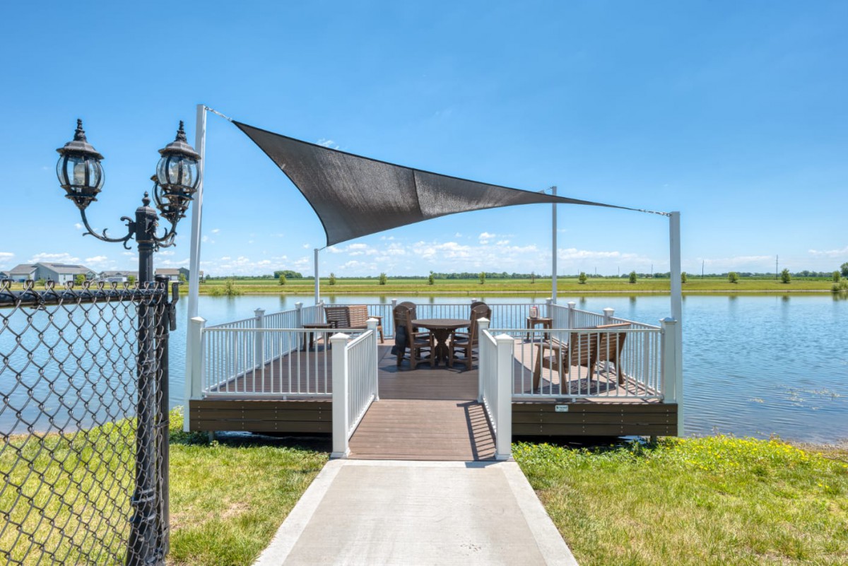 A scenic dock with comfortable seating and a shade sail on a sunny day by the lake.