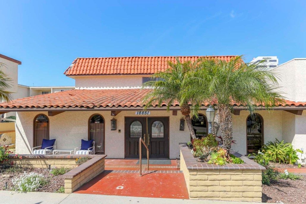 A Spanish-style house with tile roofing and palm trees at the entrance.