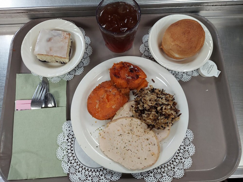 A meal served on a tray featuring turkey slices, wild rice, cooked carrots, a small sandwich, bread roll, and a drink.