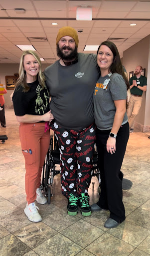 A cheerful group of friends sharing a moment together, one seated in a wheelchair and showcasing fun holiday-themed pants.