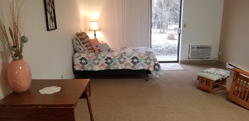 A cozy bedroom featuring a daybed with a colorful quilt, a lamp for lighting, and a window providing an outdoor view.