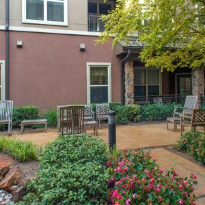 A charming outdoor patio area with chairs and lush greenery surrounded by a building.