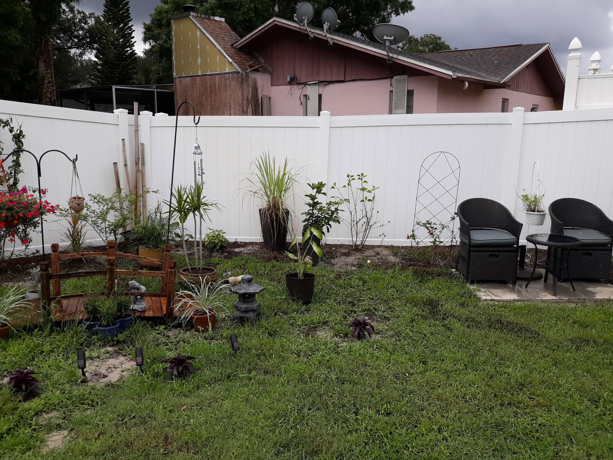 A backyard garden with various plants and a white fence, featuring outdoor seating.