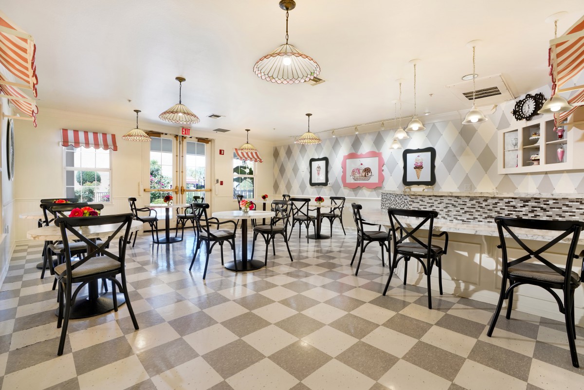 A cozy cafe interior with checkered flooring, stylish lighting, and elegant black chairs surrounding round tables.