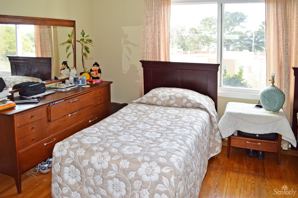 A tidy bedroom with a single bed, dresser, and large window allowing natural light to fill the room.