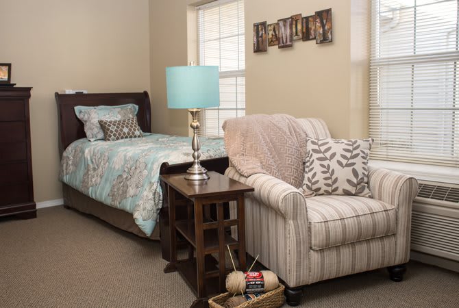 A cozy bedroom with a bed, striped armchair, and a bedside table featuring a lamp.