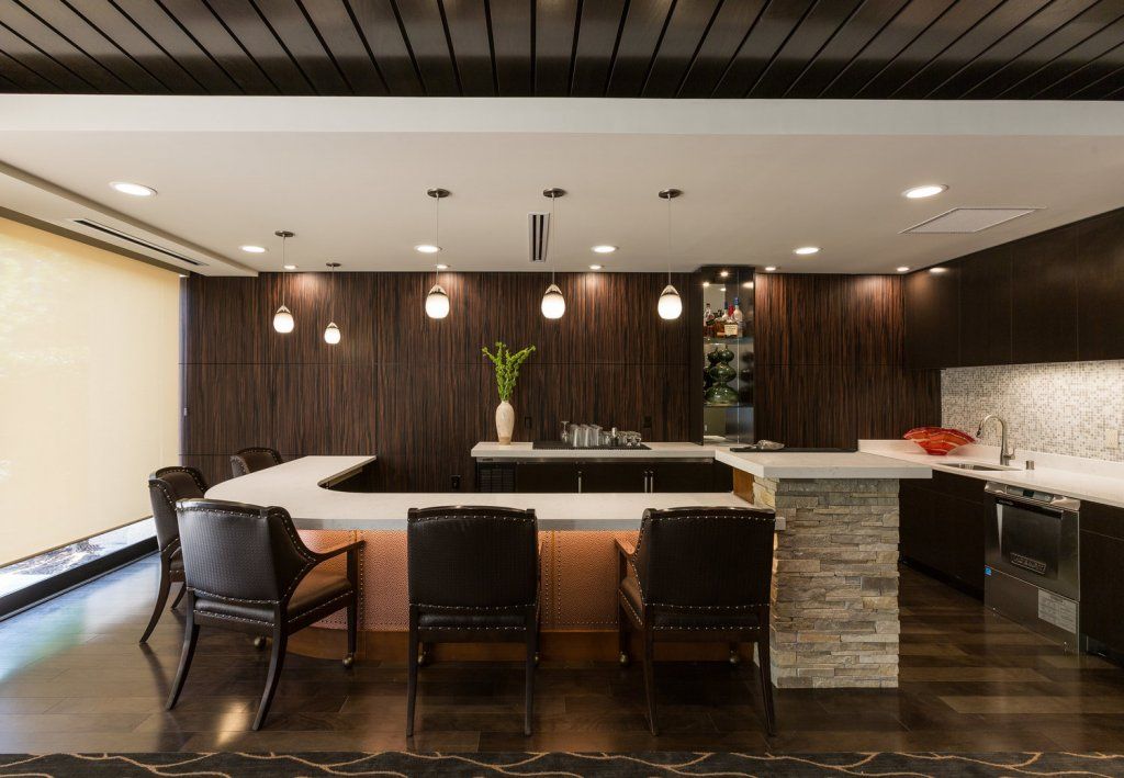 A modern kitchen with a sleek bar counter and stylish seating area, complemented by contemporary lighting.