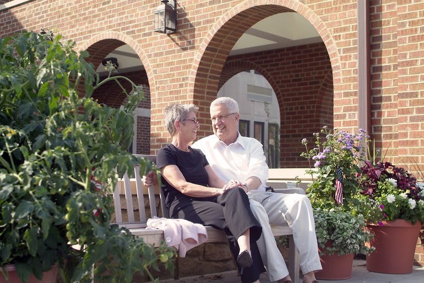 An elderly couple sitting on a bench in a garden, enjoying a conversation.