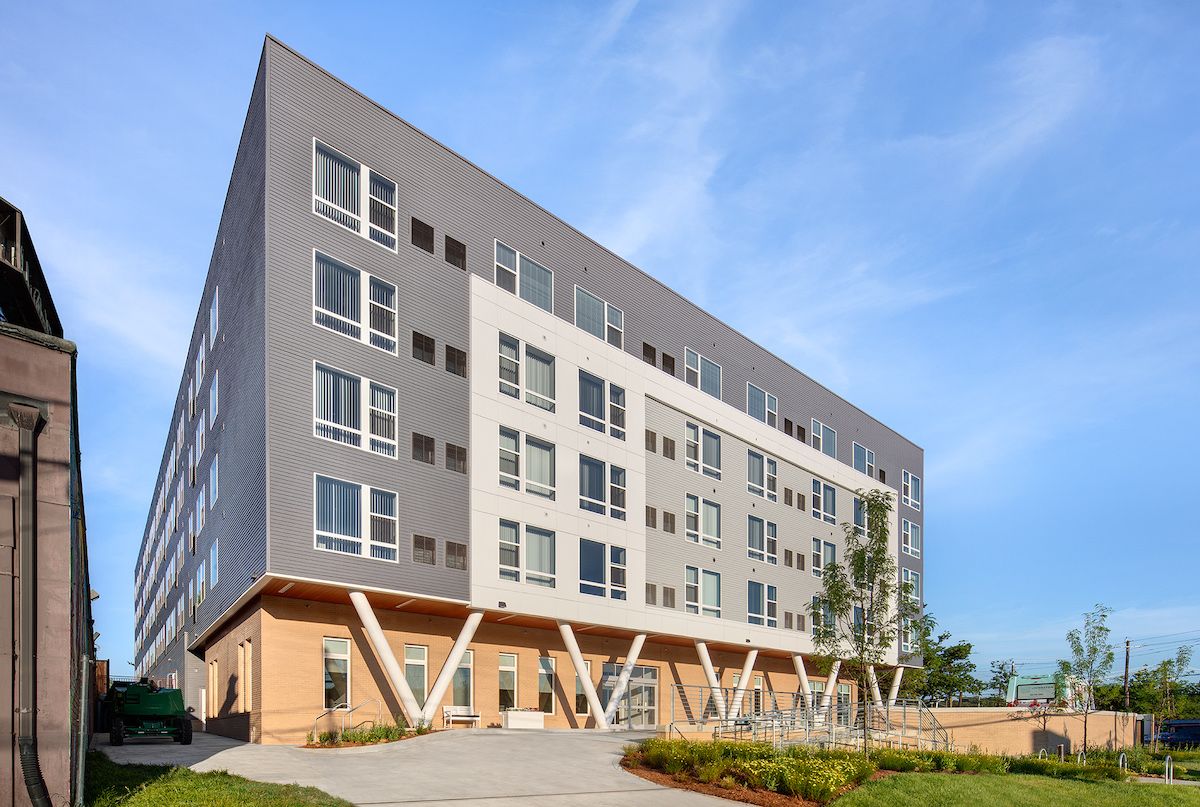A modern apartment building with a sleek design and multiple windows, set under a clear blue sky.