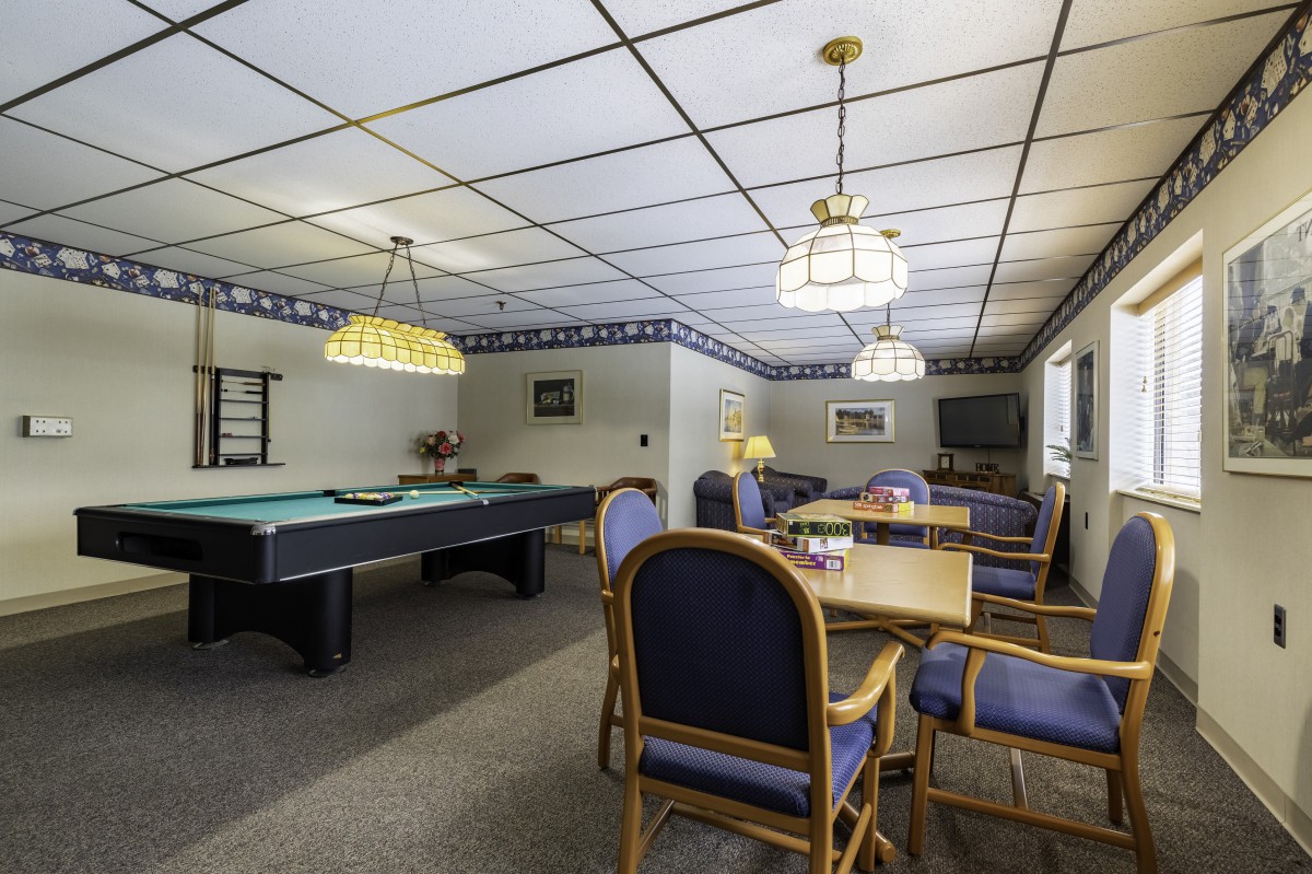 A recreational game room featuring a pool table and a seating area with chairs under decorative lighting.