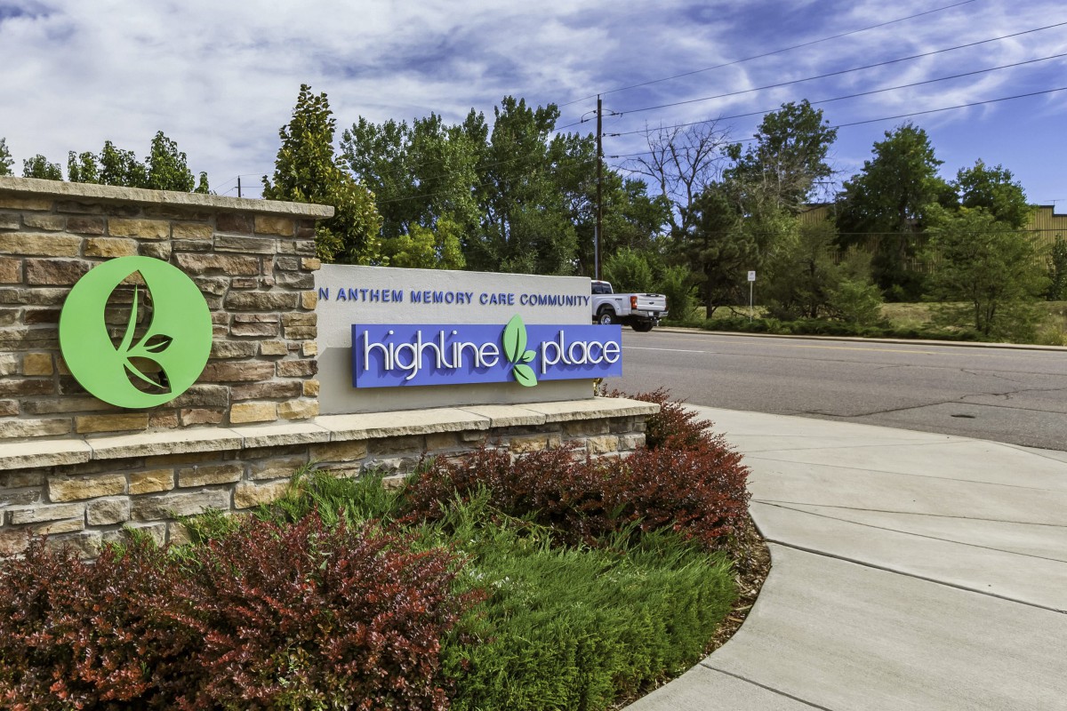 A community entrance sign surrounded by greenery and a paved pathway.