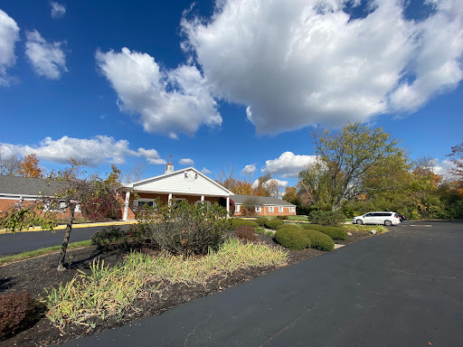 A scenic view of a house surrounded by lush greenery and a clear blue sky with fluffy clouds.