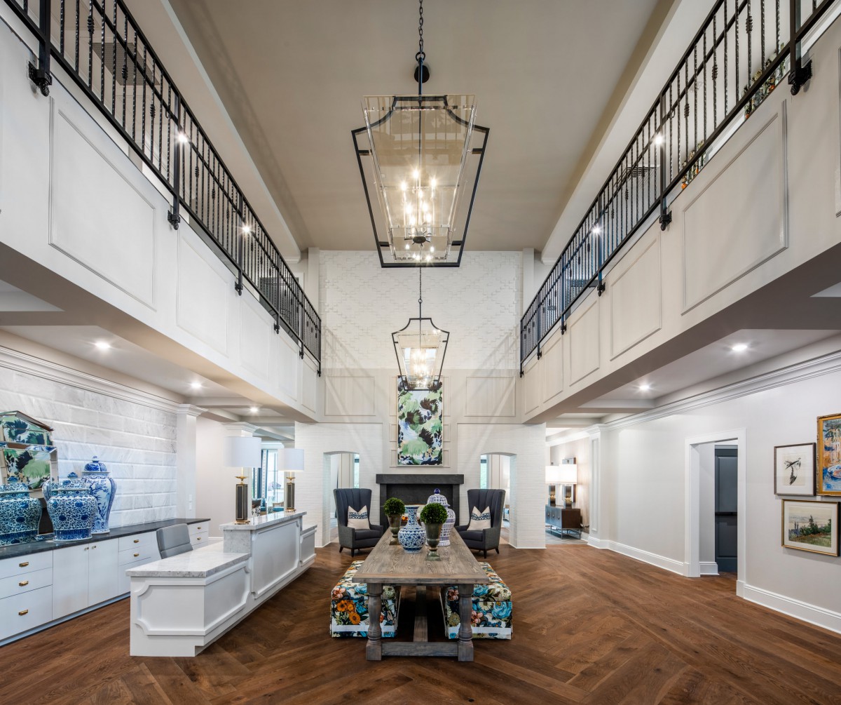 A modern dining room with high ceilings, large chandeliers, and elegant wood flooring.