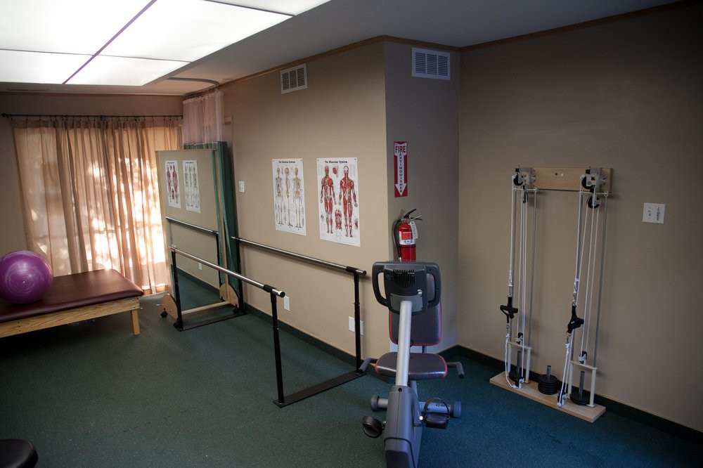 A physical therapy room equipped with exercise machines and anatomical charts on the walls.