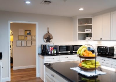 A modern kitchen with a countertop featuring a fruit basket and multiple microwaves.