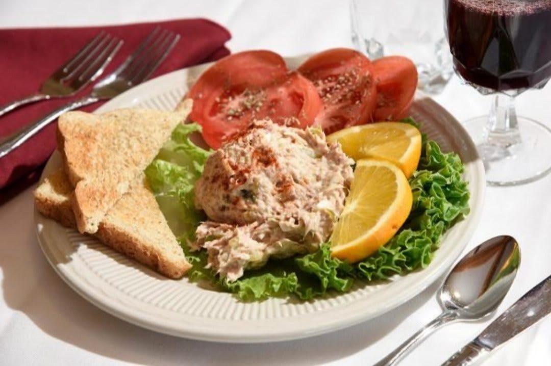 A plate of chicken salad served with sliced tomatoes, toast, and lemon wedges on a bed of lettuce.