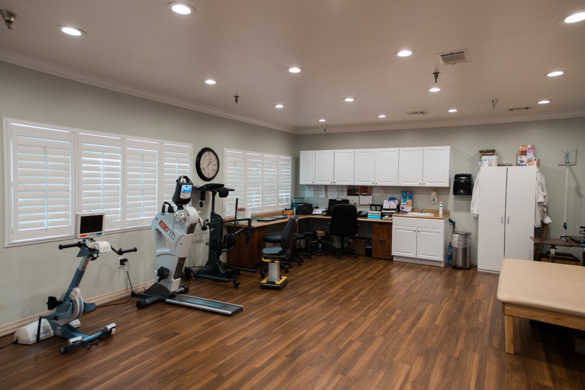 A spacious office area with exercise equipment and desks, featuring a wooden floor and white cabinetry.