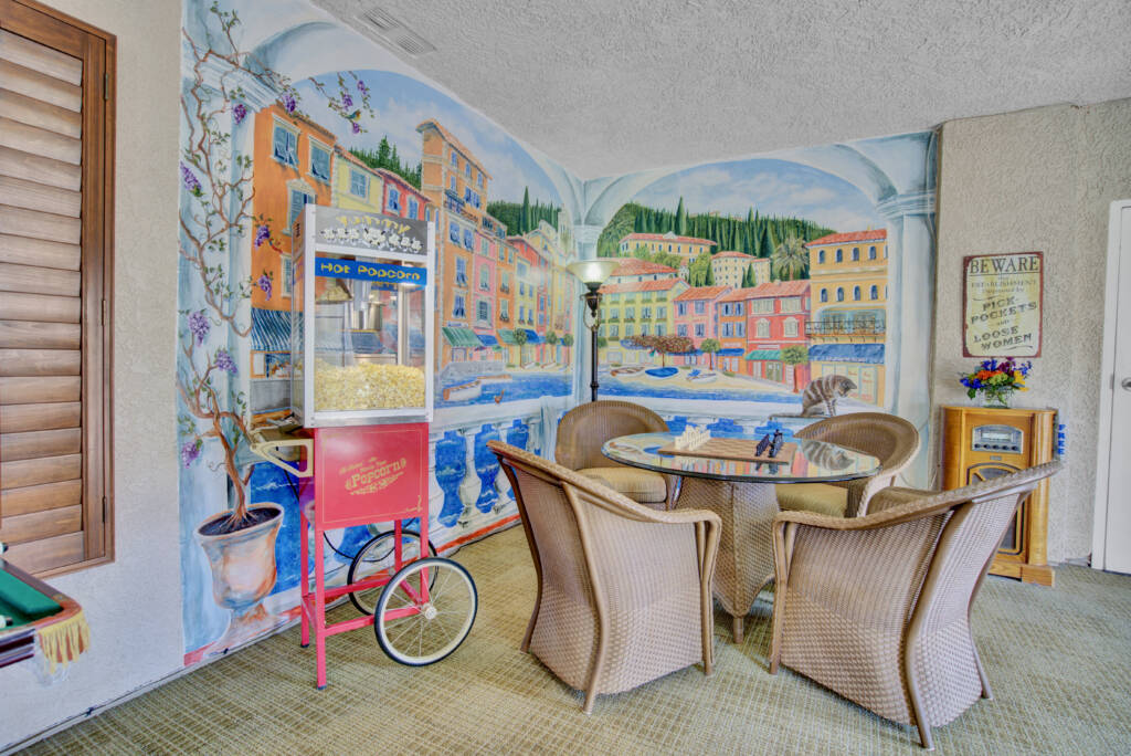 A vibrant room featuring a colorful mural, wicker chairs, a glass table, and a popcorn machine.