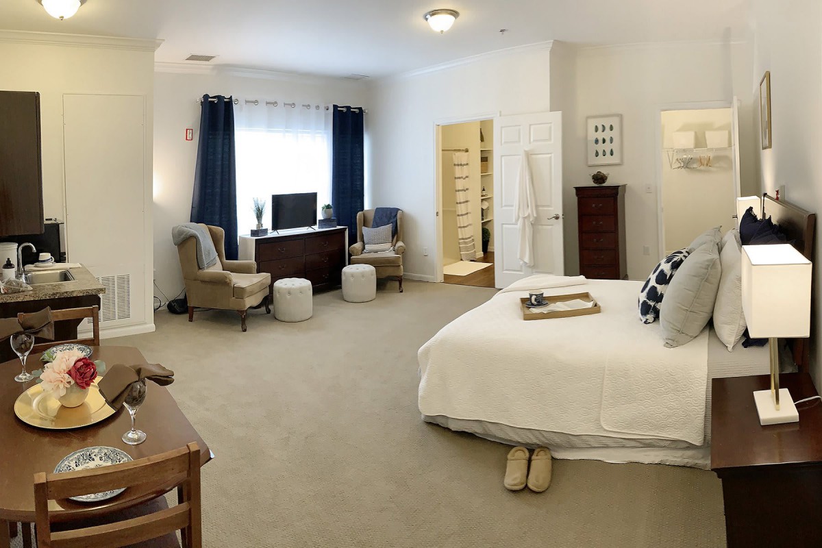 A spacious and modern bedroom with minimalist decor, featuring a comfortable bed, dresser, chairs, and a large window with curtains.