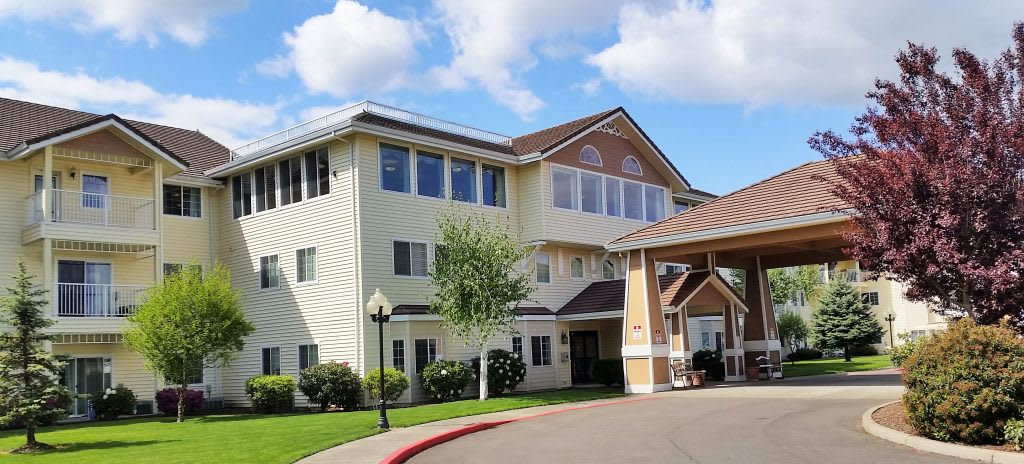 A three-story residential building with a covered entrance under a partly cloudy sky.